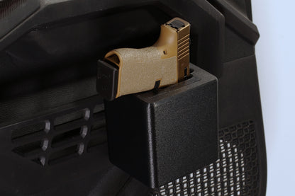 A tan and black handgun secured in a black plastic mounting holder attached to a black mesh-back office chair, shown against a light blue background.